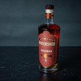 Bottle of Watershed Bourbon on a dark surface with a dark background